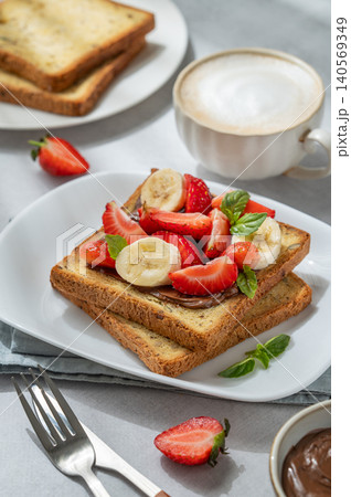 Toasted bread with chocolate cream, strawberries, and banana on a plate on a concrete background Toasted bread with chocolate cream, strawberries, and banana on a plate on a concrete background 140569349