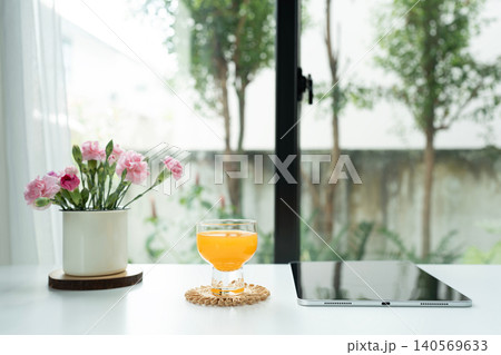 Orange juice in a glass cup and tablet and pink flowers arranged on white desk Orange juice in a glass cup and tablet and pink flowers arranged on white desk 140569633