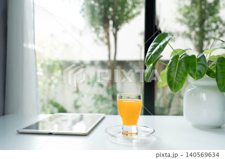 Orange juice in a glass cup and tablet and philodendron plant 140569634