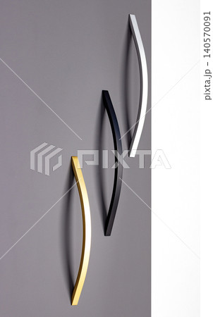 Three curved wall hooks in different colors hanging on a gray wall in a modern interior space 140570091