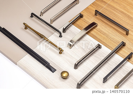 Different types of cabinet handles arranged on surfaces of wood and laminate in a workshop setting Different types of cabinet handles arranged on surfaces of wood and laminate in a workshop setting 140570110