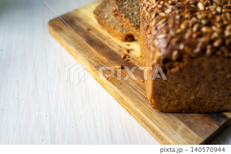Whole grain seed crusted loaf on wooden cutting board with slices and crumbs Whole grain seed crusted loaf on wooden cutting board with slices and crumbs 140570944