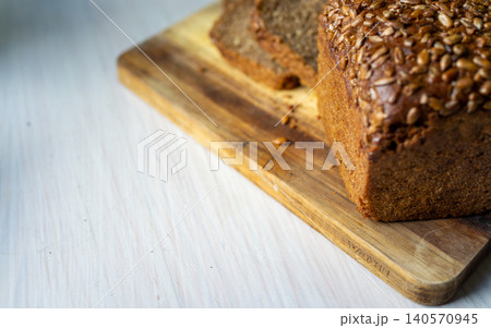 Loaf of seeded whole grain bread on wooden cutting board with sliced pieces and light tabletop Loaf of seeded whole grain bread on wooden cutting board with sliced pieces and light tabletop 140570945