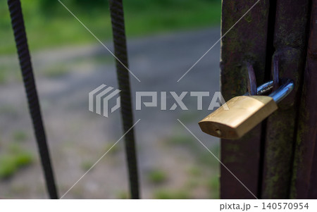 Closeup brass padlock securing rusted metal gate with blurred outdoor background Closeup brass padlock securing rusted metal gate with blurred outdoor background 140570954
