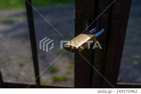Brass padlock securing outdoor metal gate with blurred background and soft natural light 140570962