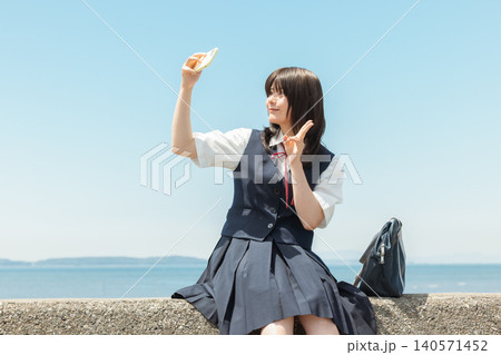 海沿いの堤防に座ってスマートフォンを操作する女子高校生 海沿いの堤防に座ってスマートフォンを操作する女子高校生 140571452