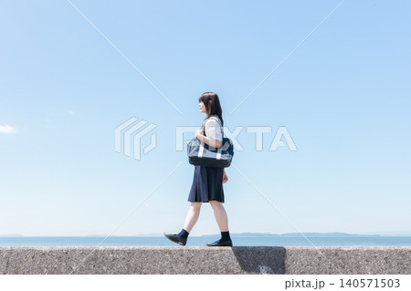 青空と海を背景に前を向いて歩く制服姿の女子高校生 140571503