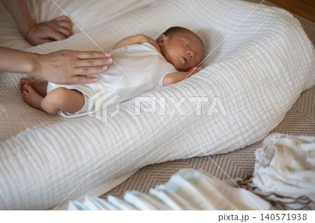 オムツや洗濯物の置いてある部屋で新生児の赤ちゃんを寝かしつけているところ オムツや洗濯物の置いてある部屋で新生児の赤ちゃんを寝かしつけているところ 140571938