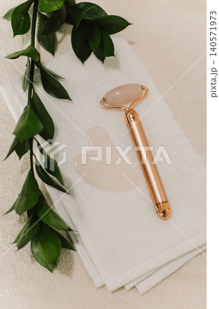 Facial rose quartz stone massage roller and gua sha massager on a white towel background. 140571973