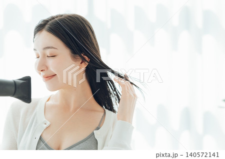 濡れた髪の毛をドライヤーで乾かす若い女性 濡れた髪の毛をドライヤーで乾かす若い女性 140572141