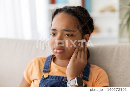 Closeup of Black teenage girl touching her ear with a worried expression Closeup of Black teenage girl touching her ear with a worried expression 140572593