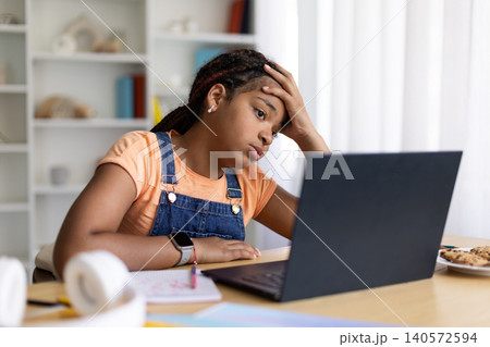Black teenage girl looking tired while studying on laptop at home 140572594