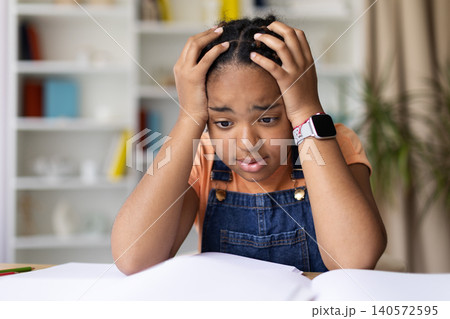 Black teenage girl holding her head in frustration while studying at home Black teenage girl holding her head in frustration while studying at home 140572595