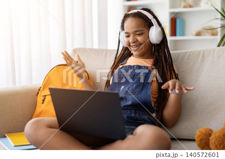 Black teenage girl participating in online video call using laptop and headphones Black teenage girl participating in online video call using laptop and headphones 140572601
