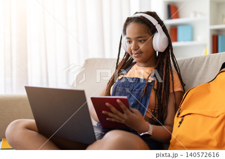 Black teenage girl studying with notebook and laptop at home Black teenage girl studying with notebook and laptop at home 140572616