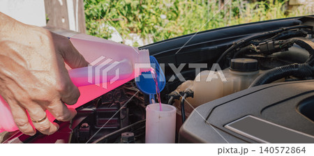 Man hand holding a plastic canister and pouring pink washer fluid into the reservoir tank under an open car hood during regular vehicle maintenance service process Man hand holding a plastic canister and pouring pink washer fluid into the reservoir tank under an open car hood during regular vehicle maintenance service process 140572864