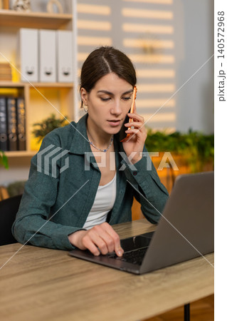 Young woman on home table talking on smartphone helping solve problem during laptop support session 140572968