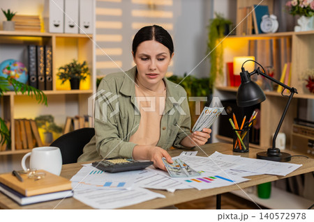 Young woman on home table managing home budget with cash calculator documents and receipts at desk Young woman on home table managing home budget with cash calculator documents and receipts at desk 140572978