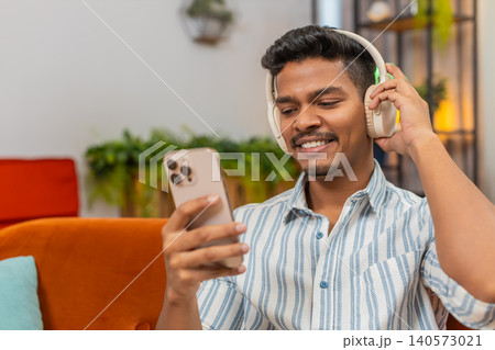 Indian man with wireless headphones tunes playlist on smartphone nods to music relax calm vibe chill Indian man with wireless headphones tunes playlist on smartphone nods to music relax calm vibe chill 140573021