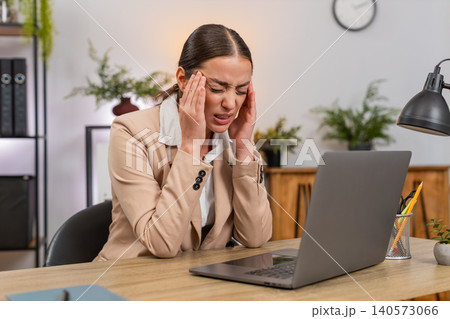 Young businesswoman rubs temples from headache while working on laptop slows down and takes breath Young businesswoman rubs temples from headache while working on laptop slows down and takes breath 140573066