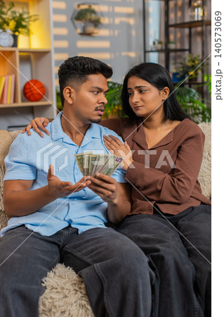Indian couple man and woman sitting on home sofa discussing small cash and home family budget stress Indian couple man and woman sitting on home sofa discussing small cash and home family budget stress 140573069