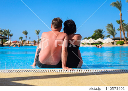 Husband and wife on vacation sitting near the pool, rear view Husband and wife on vacation sitting near the pool, rear view 140573401
