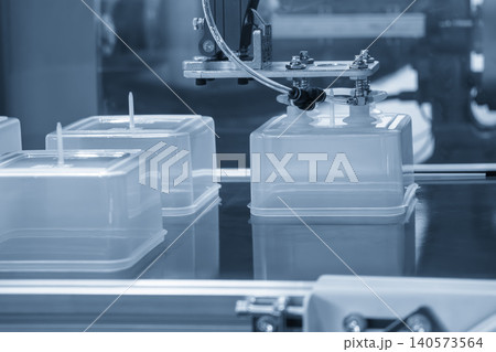 Industrial robotic arm gripping and removing a plastic box from an injection molding machine. Industrial robotic arm gripping and removing a plastic box from an injection molding machine. 140573564