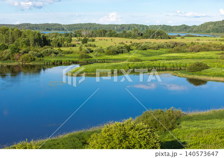 A peaceful summer landscape featuring a calm blue lake A peaceful summer landscape featuring a calm blue lake 140573647