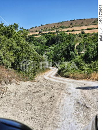 Dirt road surrounded by green trees and hills on the horizon. Dirt road surrounded by green trees and hills on the horizon. 140573968