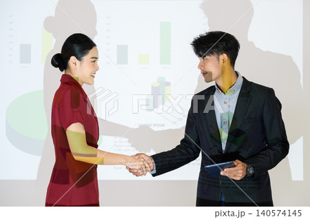 business partners shaking hands after concluding a business presentation finished. Business man and woman standing in front of Infographics Animation on Big Screen. Business to succeed concept. 140574145