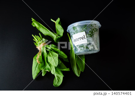 Green sorrel herb bunch with plastic container on black background Green sorrel herb bunch with plastic container on black background 140574401
