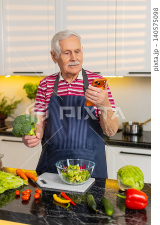 Senior old man using smartphone to check grocery list while preparing healthy meal in home kitchen Senior old man using smartphone to check grocery list while preparing healthy meal in home kitchen 140575098