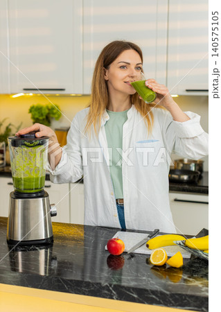 Middle-aged woman sipping green smoothie in home kitchen for healthy diet weight loss detox routine Middle-aged woman sipping green smoothie in home kitchen for healthy diet weight loss detox routine 140575105