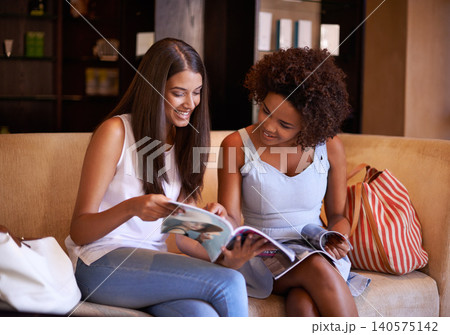 Friends, sofa and reading magazine in living room for print media entertainment, discussion and bonding. Women, couch and paper with conversation for knowledge, gossip story or information at home Friends, sofa and reading magazine in living room for print media entertainment, discussion and bonding. Women, couch and paper with conversation for knowledge, gossip story or information at home 140575142