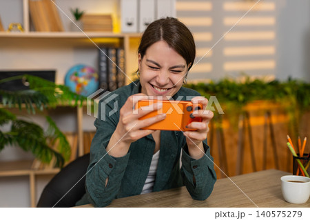Young woman on home table winning mobile game on smartphone feeling happy during online play at desk Young woman on home table winning mobile game on smartphone feeling happy during online play at desk 140575279
