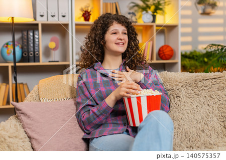 Young woman on home sofa watching fun film with popcorn laughing in surprise during home movie night Young woman on home sofa watching fun film with popcorn laughing in surprise during home movie night 140575357