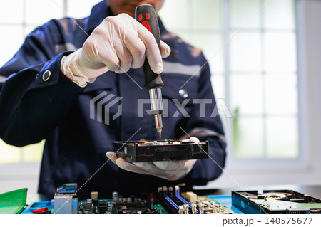 Technician in gloves repairs a computer hard drive with a screwdriver over an open motherboard in a bright workshop, showing data recovery, maintenance and hardware service. Technician in gloves repairs a computer hard drive with a screwdriver over an open motherboard in a bright workshop, showing data recovery, maintenance and hardware service. 140575677