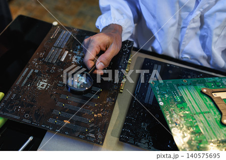 Close-up of a technician inspecting computer circuit boards with a magnifying glass on a workbench, showing electronics repair, quality control, and hardware maintenance. 140575695