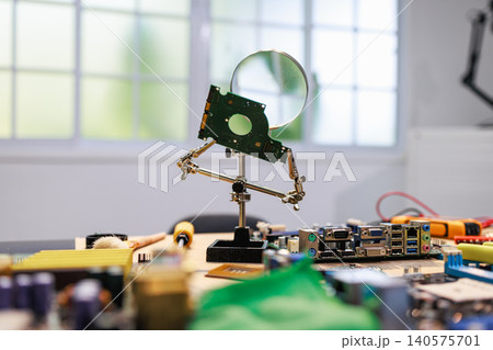 Magnifying glass holding a hard drive part above computer motherboard parts on a workbench in a bright electronics repair workspace. Magnifying glass holding a hard drive part above computer motherboard parts on a workbench in a bright electronics repair workspace. 140575701