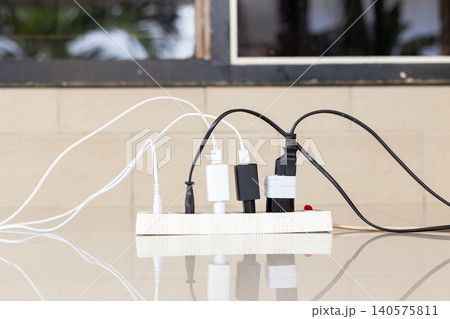Close-up of an overloaded power strip with multiple plugs and tangled wires, representing electrical fire hazards and domestic safety risks Close-up of an overloaded power strip with multiple plugs and tangled wires, representing electrical fire hazards and domestic safety risks 140575811