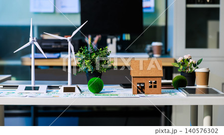 Small house model with wind turbines and green plants on an office table, showing clean energy, sustainable living and eco home planning in a modern workspace. Small house model with wind turbines and green plants on an office table, showing clean energy, sustainable living and eco home planning in a modern workspace. 140576302