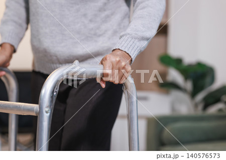 Close-up of an older adult using a walker at home, showing support, mobility, recovery, and daily care in a calm indoor setting. 140576573