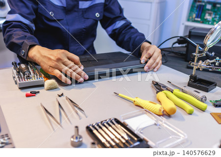 Technician repairs a laptop at a workbench with screwdrivers, pliers and precision tools in an electronics workshop. Technician repairs a laptop at a workbench with screwdrivers, pliers and precision tools in an electronics workshop. 140576629