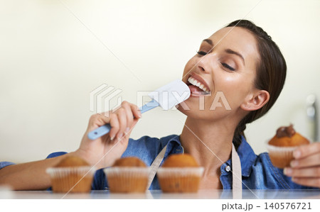 Baking, cupcakes and woman with spatula in kitchen tasting sweet chocolate frosting for dessert. Cooking, eating and young female baker working on muffins and licking tool at home or apartment. 140576721