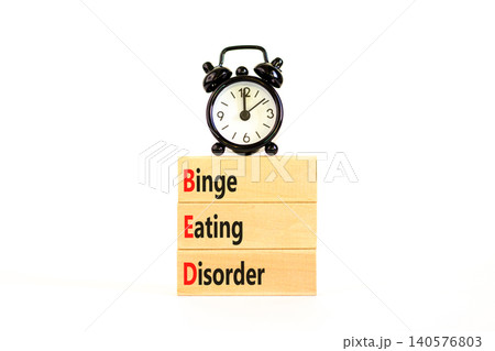 BED binge eating disorder symbol. Concept words BED binge eating disorder on beautiful wooden blocks. Beautiful white background. Alarm clock. Medical BED binge eating disorder concept. Copy space. BED binge eating disorder symbol. Concept words BED binge eating disorder on beautiful wooden blocks. Beautiful white background. Alarm clock. Medical BED binge eating disorder concept. Copy space. 140576803
