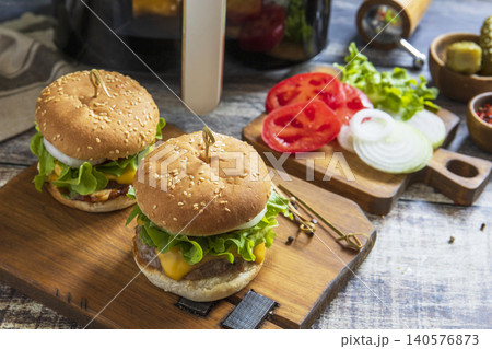 Two savory delicious homemade cheeseburger in kitchen gadget modern air fryer on wooden background. Lifestyle trendy of new cooking. Copy space. Two savory delicious homemade cheeseburger in kitchen gadget modern air fryer on wooden background. Lifestyle trendy of new cooking. Copy space. 140576873