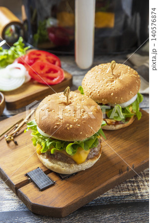 Two savory delicious homemade cheeseburger in kitchen gadget modern air fryer on wooden background. Lifestyle trendy of new cooking. Copy space. Two savory delicious homemade cheeseburger in kitchen gadget modern air fryer on wooden background. Lifestyle trendy of new cooking. Copy space. 140576874
