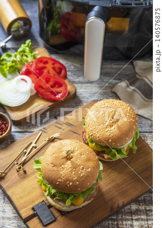 Two savory delicious homemade cheeseburger in kitchen gadget modern air fryer on wooden background. Lifestyle trendy of new cooking. Two savory delicious homemade cheeseburger in kitchen gadget modern air fryer on wooden background. Lifestyle trendy of new cooking. 140576875
