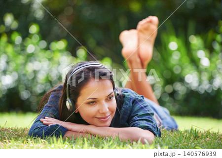 Grass, thinking and woman with headphones, relax and streaming music with peace, sound and sunshine. Person in a park, outdoor and girl with headset and podcast with radio and weekend break in garden 140576939