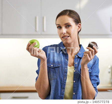 Woman, portrait and choice with apple, cupcake and decision in health and wellness at home. Face of female person with organic green fruit and chocolate muffin for diet or option in kitchen at house Woman, portrait and choice with apple, cupcake and decision in health and wellness at home. Face of female person with organic green fruit and chocolate muffin for diet or option in kitchen at house 140577278